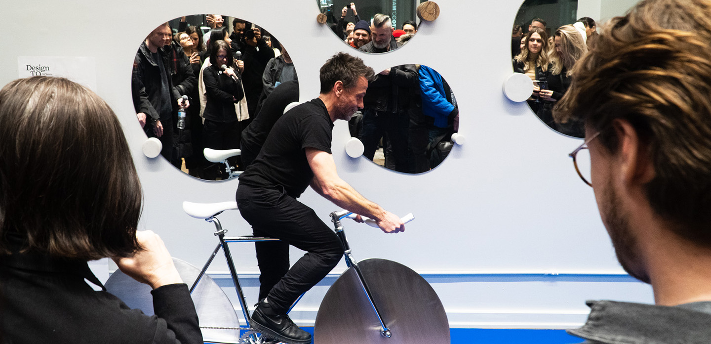 Photo of a DesignTO exhibition indoors with attendees playing a game with a spinning wheel.