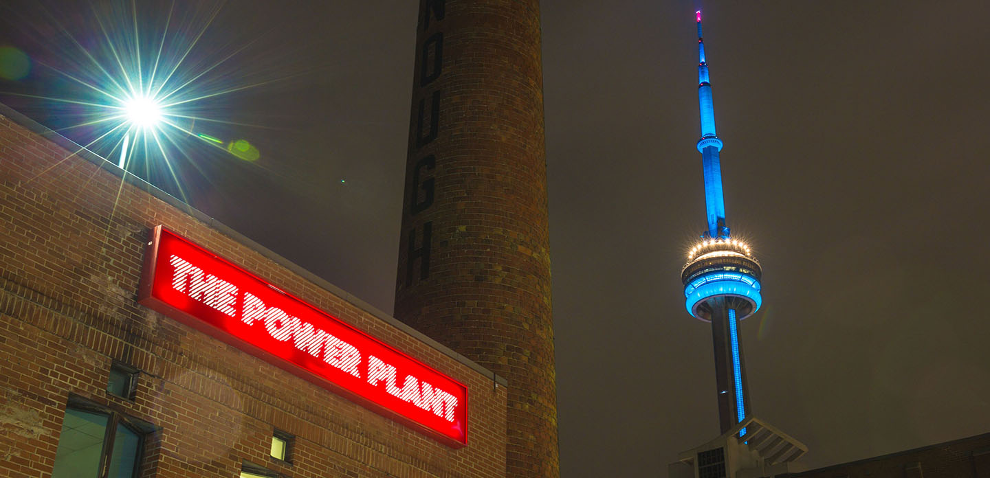 Photo of the Power Plant from outside at night with the CN tower in the background.